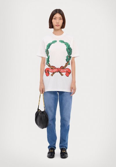 Bílý bavlněný tričko s grafikou zeleného vavřínového věnce a červeným textem "MOSCHINO," kombinováno s modrými džíny a černou kabelkou.