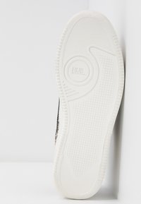 Semelle de basket en caoutchouc blanc avec un motif antidérapant texturé, présentant un logo circulaire embossé "HUB". Le côté est noir avec un motif décoratif.