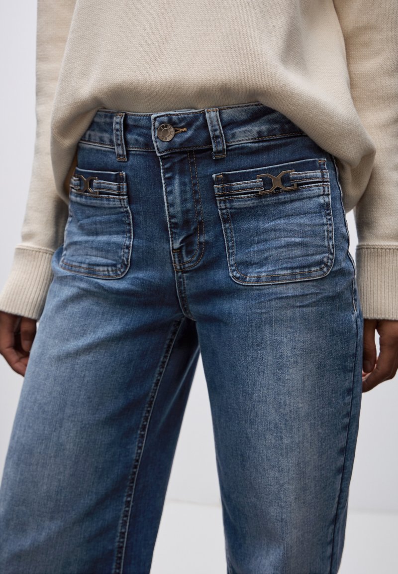 Jeans in denim chiaro con una vestibilità rilassata, dotati di due tasche anteriori e dettagli decorativi sulle tasche posteriori.