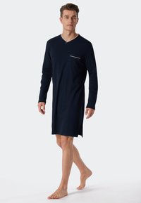 Marineblauwe lange nachthemd van zacht katoen, met een V-hals en een kleine borstzak met witte accentpiping. Zijsplitten voor extra comfort.