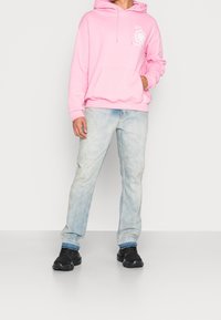 Sudadera con capucha rosa y bolsillo frontal, con un gráfico de flores; combinada con jeans azul claro y zapatillas negras.