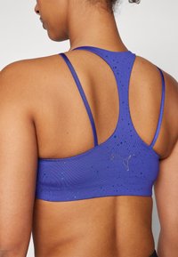 Paarse sport-bh met racerback-ontwerp, een gladde textuur en verspreide accenten in lichtere tinten. Inclusief een zilverkleurig logo-detail.