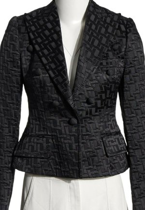 Blazer negro texturizado de doble botonadura con patrón geométrico, hombros acolchados y botones cubiertos de tela, llevado sobre pantalones blancos.