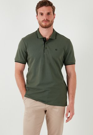 Polo en verde oliva, fabricado con un tejido texturizado, cuenta con un cuello negro y una tapeta de tres botones, con un logo sutil en el pecho.