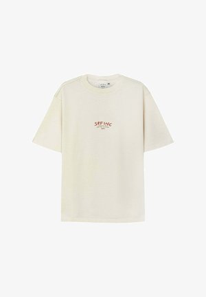 Beżowa koszulka z krótkim rękawem z czerwonym napisem "SRFNC" oraz mniejszym tekstem poniżej na wysokości klatki piersiowej, okrągły dekolt, widoczna metka w średnim rozmiarze.