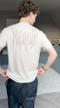 Bež majica kratkih rukava s velikim svijetlim natpisom "Napapijri" na leđima. Uparena s tamnim trapericama.