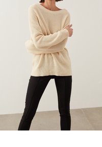 Suéter de punto beige claro con un corte holgado, escote ancho y mangas largas, combinado con pantalones negros ajustados. Tejido texturizado.