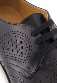 Zwarte leren schoen met geperforeerde details en grijze veters. Heeft een gladde afwerking en een lichtbruine binnenzool die aan de binnenkant zichtbaar is.