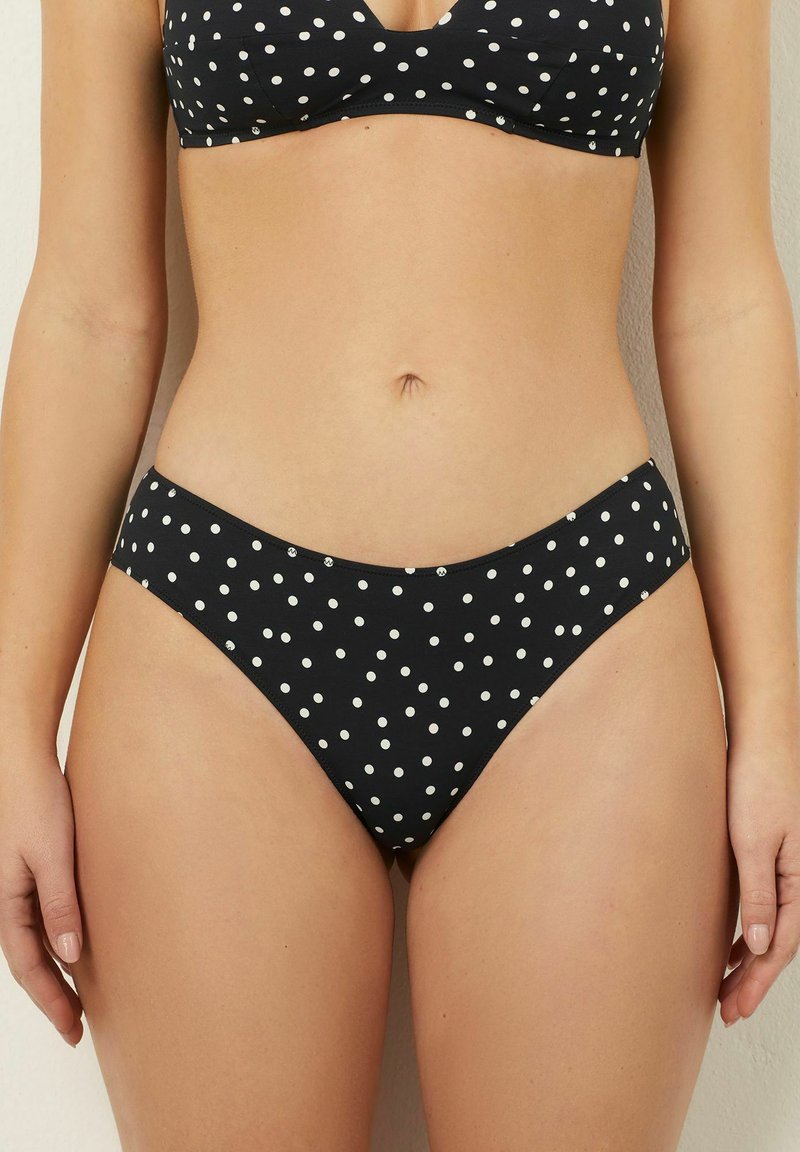 Czarny dół bikini w białe grochy, niski krój, gładka faktura i minimalne zakrycie. Charakteryzuje się prostym, bezszwowym krojem.