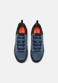 Niebieskie siatkowe sneakersy z czarnymi akcentami, teksturowanymi powierzchniami i pomarańczową podszewką. Odbijające światło logo Adidas z boku, czarne sznurówki i pętla do zakupu.