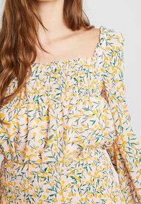 Vaaleanpunainen paita, jossa on smokkaukset neliönmuotoisessa kaula-aukossa ja pitkissä hihoissa. Kukkakuosisessa on keltaisia marjoja ja vihreitä lehtiä. Pehmeä, kevyt kangas.