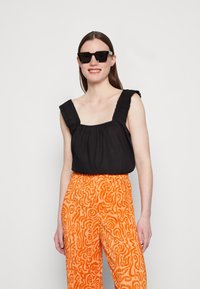 Top preto sem mangas com alças franzidas, combinado com calças largas laranja com um padrão em espiral. Design simples e casual.
