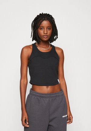 Top corto a costine nero con dettaglio a cucitura ondulata, abbinato a pantaloni della tuta grigi. Il tessuto è morbido e il top ha un design aderente.