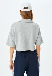 Grå cropped sweatshirt med korte ærmer og krave, parret med marineblå bukser med elastisk talje. Stoffet ser blødt ud med en glat tekstur.