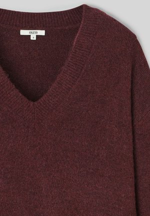 Pull en V bordeaux en maille douce. Doté d'un col et d'un ourlet côtelés, il présente une texture lisse et un design simple. Taille S.