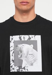 Camiseta negra con un destacado gráfico blanco de un oso polar rugiente dentro de un marco cuadrado con textura agrietada y el texto "BOSS".