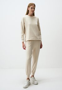Completo felpa e pantaloni jogger in tessuto morbido; vestibilità relaxed, polsini a costine su entrambi, caratterizzati da cuciture laterali discrete. Abbinato a sneaker bianche.