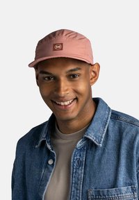 Gorra rosa con visera curva y un parche con logo, llevada por una persona con chaqueta de mezclilla. Tela suave, diseño flexible, aspecto casual.