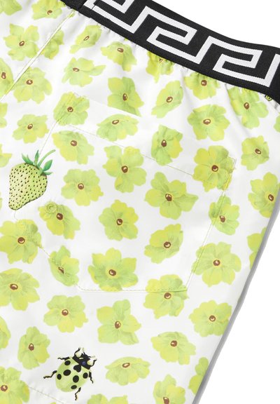 Pantaloni corti in tessuto bianco con un vivace motivo di fiori verdi, una fragola contornata di giallo e una coccinella con macchie nere. Vita nera.
