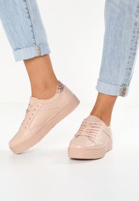 Ljusrosa sneakers i syntetmaterial, med en texturerad yta och glittrande detaljer på hälen. Rund tå och snörningsdesign.