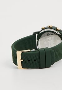 Grön silikonarmband med en strukturerad yta, försett med en guldfärgad metallspänne och guldaccenter på urtavlan.