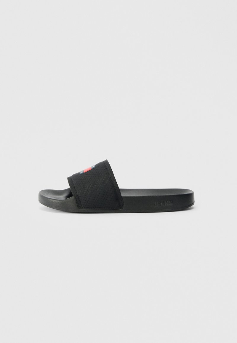 Black slide sandal with textured strap featuring small red and blue logo and contoured footbed, side embossed with "JEANS" text.
