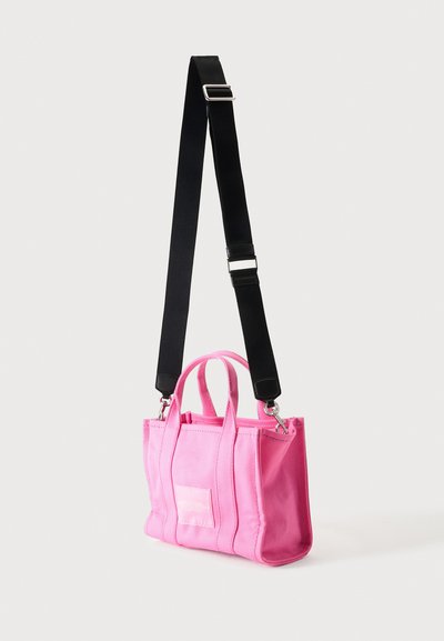 Sac cabas rectangulaire rose avec deux poignées courtes et une bandoulière noire réglable et amovible sur fond uni.