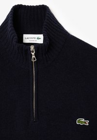 Navy blue knit sweater with a high ribbed collar, silver zipper, and embroidered green crocodile logo on the left chest. Classic fit.