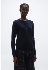 Tmavomodrý kardigán z mäkkej látky, s okrúhlym výstrihom, dlhými rukávmi a radom gombíkov na prednej strane.