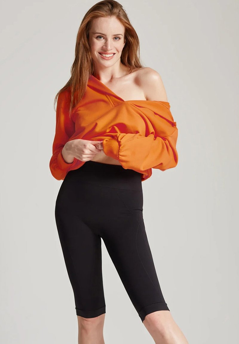 Pomarańczowy, opuszczony na ramiona sweter i czarne legginsy do kolan; miękki materiał o nieco luźnym kroju i gładkiej fakturze.