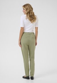 Pantalons légers de couleur vert olive avec une taille élastique, deux poches arrière et une coupe fuselée, associés à un haut blanc ajusté.
