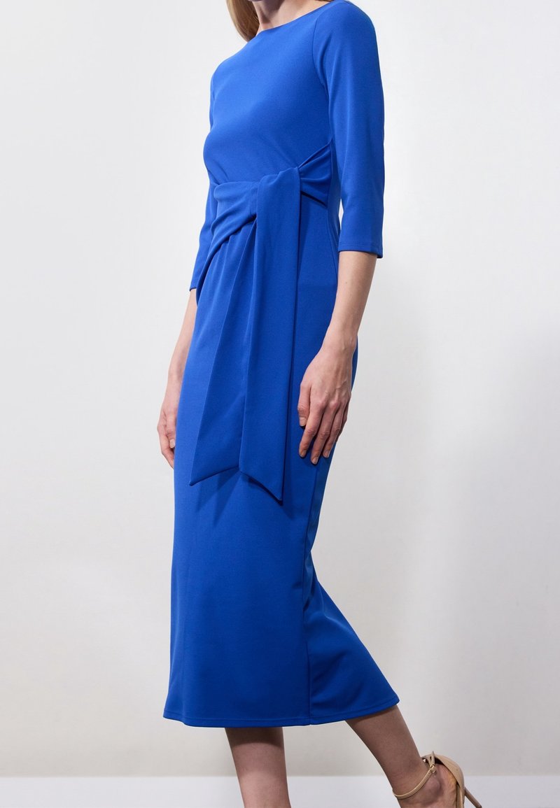 Robe midi bleue avec des manches trois-quarts, une ceinture à la taille, une texture de tissu lisse et une silhouette ajustée. Avec un col rond simple.
