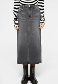 Dunkelgrauer Jeans-Maxikleid, mit vorderen Taschen, geradem Schnitt und Gürtelschlaufen. Kombiniert mit schwarzen Knöchelstiefeln und einem gestreiften Oberteil.