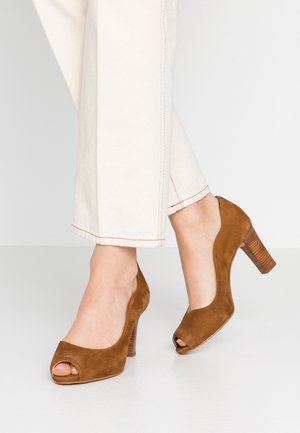 Brune ruskind peep-toe højhælede sko med stablede træblk hæle, båret med off-white bukser med lige ben.