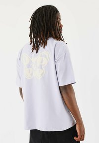 Camiseta de algodón de gran tamaño en lavanda clara con un gran gráfico de mariposa amarilla en la espalda, con mangas cortas y un corte relajado.