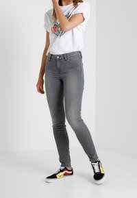 Jeans ajustados grises con una textura suave, combinados con una camiseta gráfica blanca y zapatillas negras con acentos de llamas de colores.