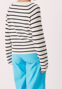 Gestreepte trui in marineblauw en crème, met geribbelde zoom, lange mouwen, gecombineerd met felblauwe broek, met een ontspannen pasvorm.