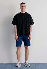 Tricou negru supradimensionat cu mânecă scurtă, pantaloni scurți din denim albastru și pantofi sport gri-albi. Design simplu cu o croială lejeră.