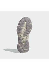 Sulan på en sneaker, med en strukturerad ljusgrå plastyta som har olika spår och kanter för grepp och dämpning.