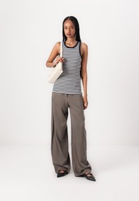 Black and white striped tank top, gray wide-leg trousers, and black pointed flats. Holding a small beige handbag. Smooth textures.