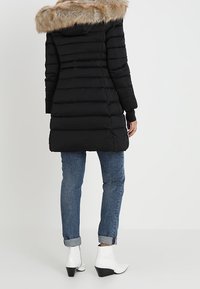 Musta toppatakki, jossa tekoturkiskaulus, pitkät hihat ja pystyt ompeleet, yhdistetty sinisiin farkkuihin ja valkoisiin nilkkureihin.