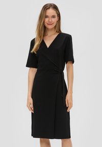 Robe noire portefeuille en tissu doux avec un décollet�é en V, des manches courtes et un détail de nouage sur le côté. Longueur genou avec une texture lisse.