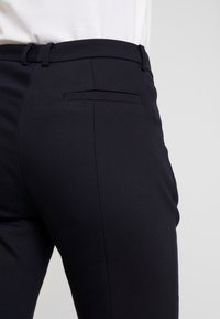 Pantalons noirs ajustés en tissu lisse, au design slim-fit, avec une poche arrière et une passante pour ceinture à la taille.