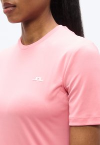 Ροζ αθλητική μπλούζα με κοντά μανίκια και στρογγυλή λαιμόκοψη. Διαθέτει λευκό λογότυπο στο αριστερό μέρος του στήθους και απαλό, ελαστικό ύφασμα.