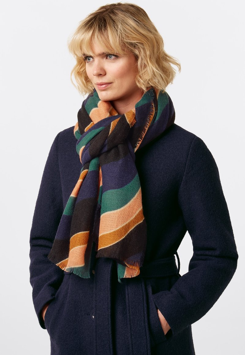 Multifarbener gestreifter Schal mit Grüntönen, Orange und Marineblau, mit einer weichen Textur und fransigen Kanten, über einem dunklen Mantel getragen.