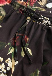 Lilledega kangas, kus on erksad roosid ja rohelus mustal taustal. Elastne vöökoht trossi kinnitamiseks reguleerimiseks.