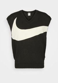 Černý bezrukávový pulovr s výstřihem do V a velkým bílým logem Nike swoosh přes přední stranu, vyrobený z měkké pleteniny, s žebrovaným lemem.