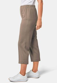 Bruine, cropped broek met een gevoeld stof en een elastische tailleband, gecombineerd met witte sneakers. Heeft een rechte snit met zijopeningen aan de zoom.