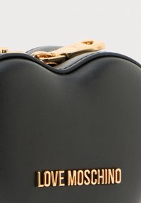 Fekete műbőr táska ívelt tetővel, arany cipzárral és arany fémes betűkkel készült "LOVE MOSCHINO" logóval. Simább textúrával.