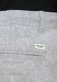 Γκρι υφασμάτινο πλεκτό με διακριτικό σχέδιο, που διαθέτει τσέπη με φερμουάρ και λευκή ετικέτα με το κείμενο "JACK & JONES" και "EST. 1990".